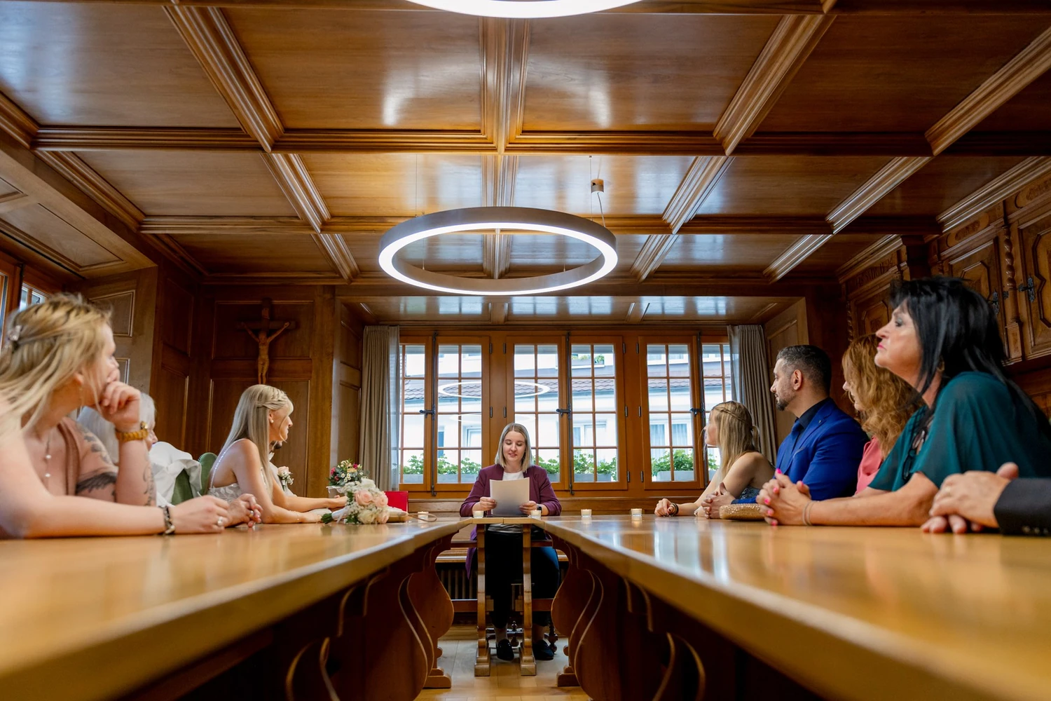 Blick von der Tür in den getäfelten Trausaal mit langer Tafel, Lichtring und Gästen zu beiden Seiten
