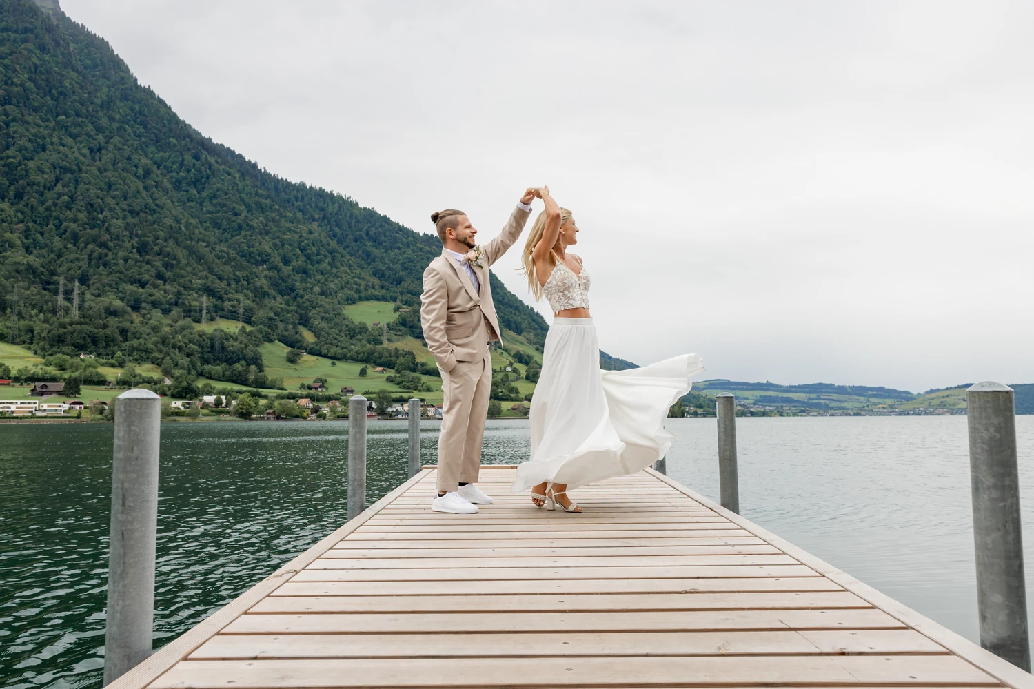 Bräutigam dreht die Braut auf einem Holzsteg im Zugersee, dahinter der bewaldete Hang