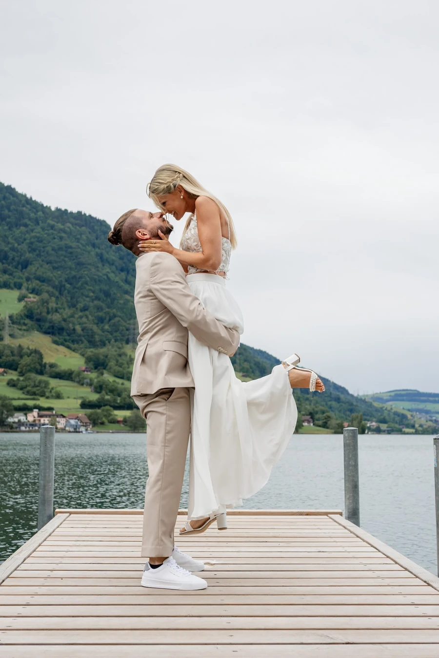 Brautpaar auf einem Steg am Zugersee, die Braut wird angehoben, im Hintergrund die Berge