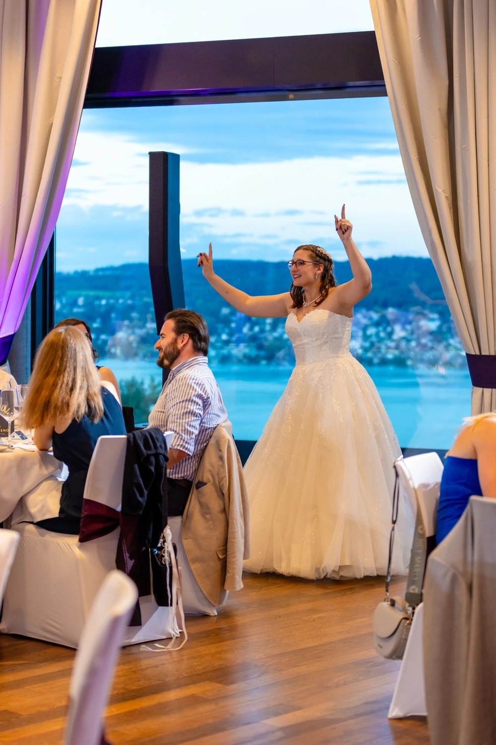 Braut tanzt vor der Panoramascheibe des Saals, dahinter der Zürichsee