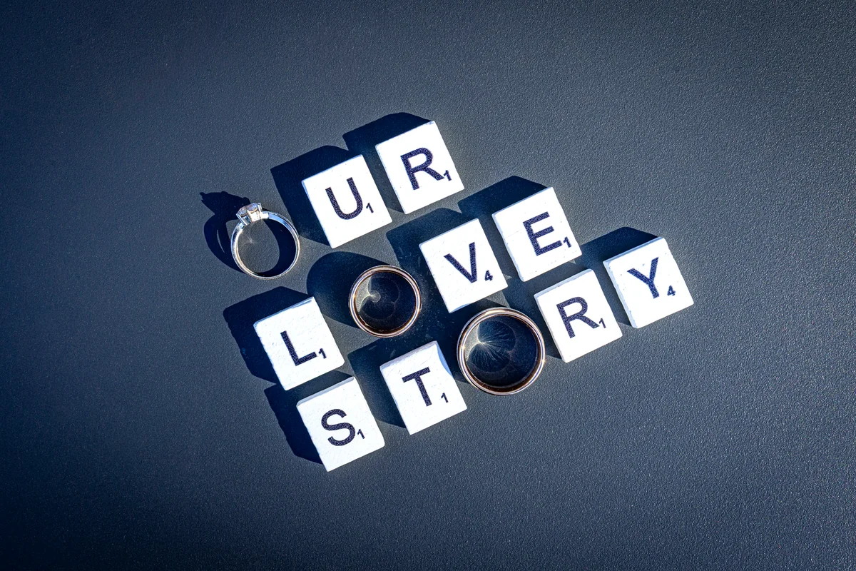 Eheringe liegen auf Buchstabensteinen, die die Worte Our Love Story ergeben
