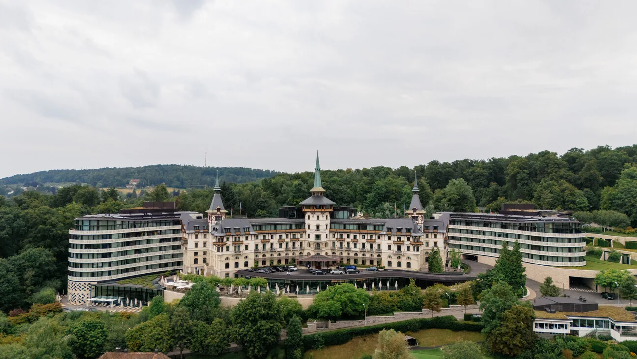 Das Dolder Grand von vorn aus der Luft, dahinter der bewaldete Hang