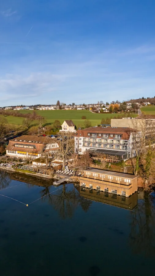 Dasselbe Resort im Hochformat, davor spiegelt sich das Gebäude im ruhigen Wasser