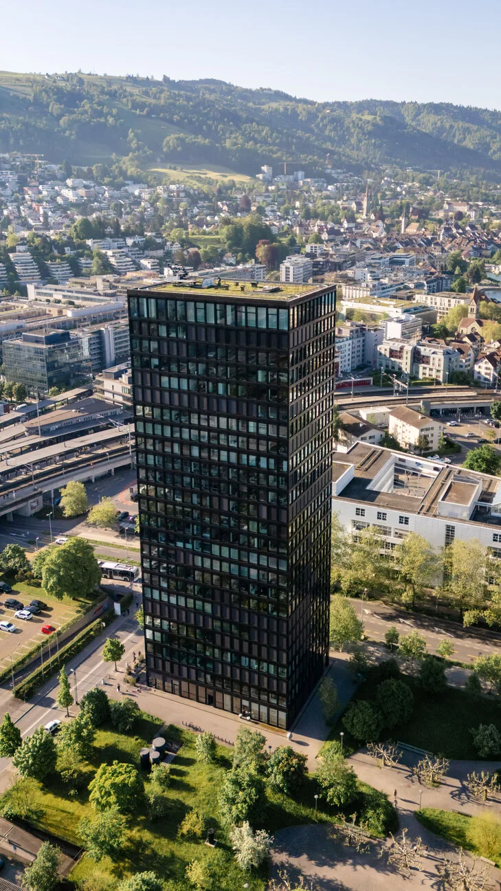 Der Park Tower in Zug im Hochformat, dahinter Stadt und Hügelzug