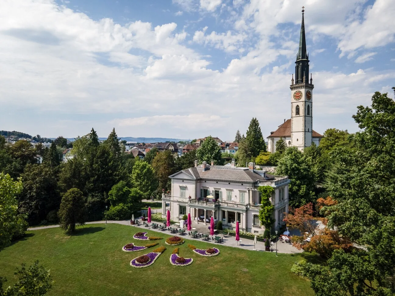 Luftaufnahme über Cham mit der Villa Villette, dem Kirchturm und Blumenbeeten im Park
