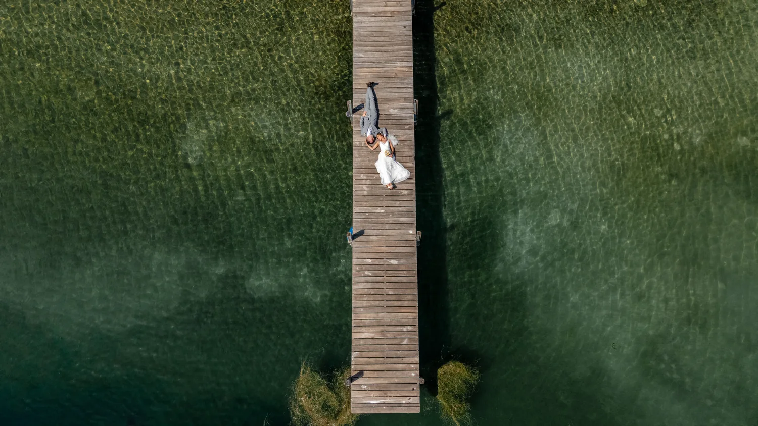 Weites Bild von oben: Brautpaar auf einem Steg über flachem Wasser, der Grund ist durch die Oberfläche zu sehen