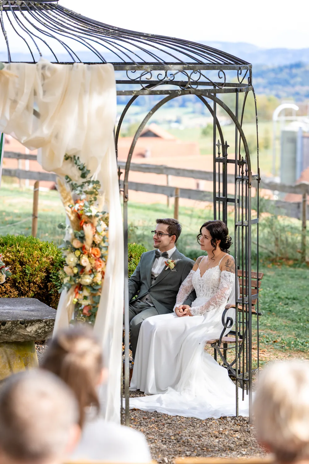 Brautpaar sitzt während der freien Trauung im Pavillon mit Blumenbogen