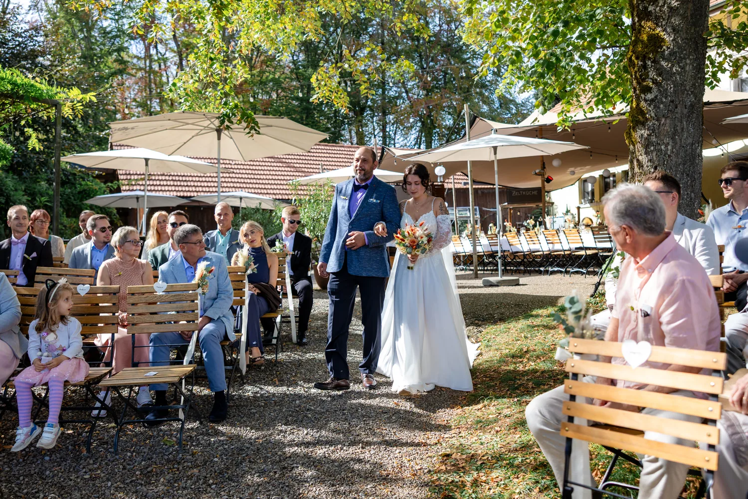 Einzug der Braut zur Trauung zwischen den Stuhlreihen im Garten