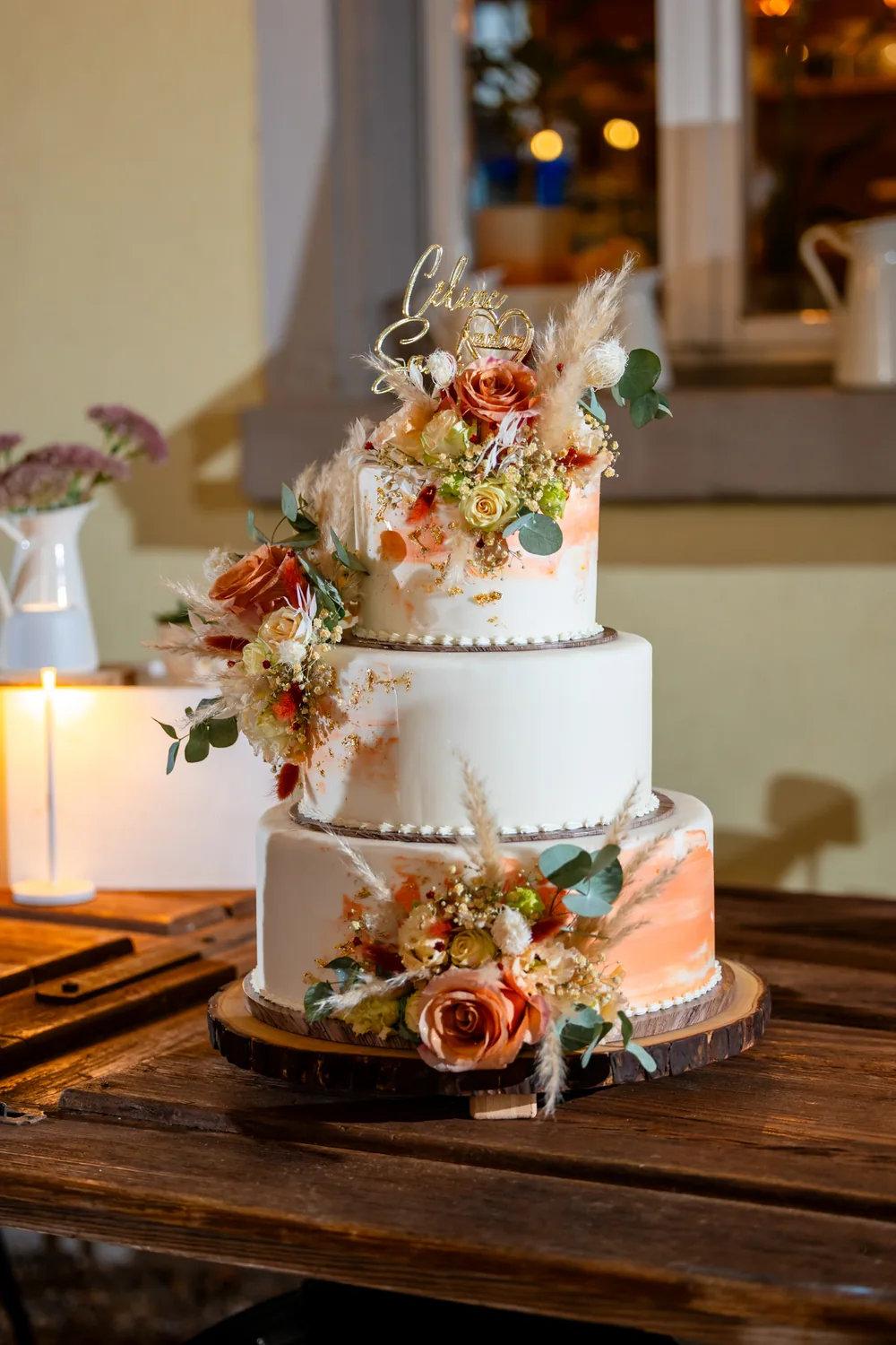 Dreistöckige Hochzeitstorte mit Blumen auf einem Holztisch bei Kerzenlicht