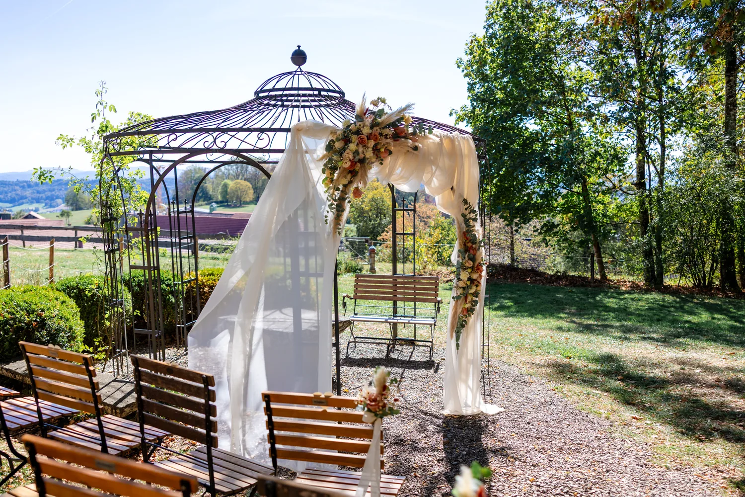 Schmiedeeiserner Pavillon im Garten mit Blumenbogen und hellen Stoffbahnen