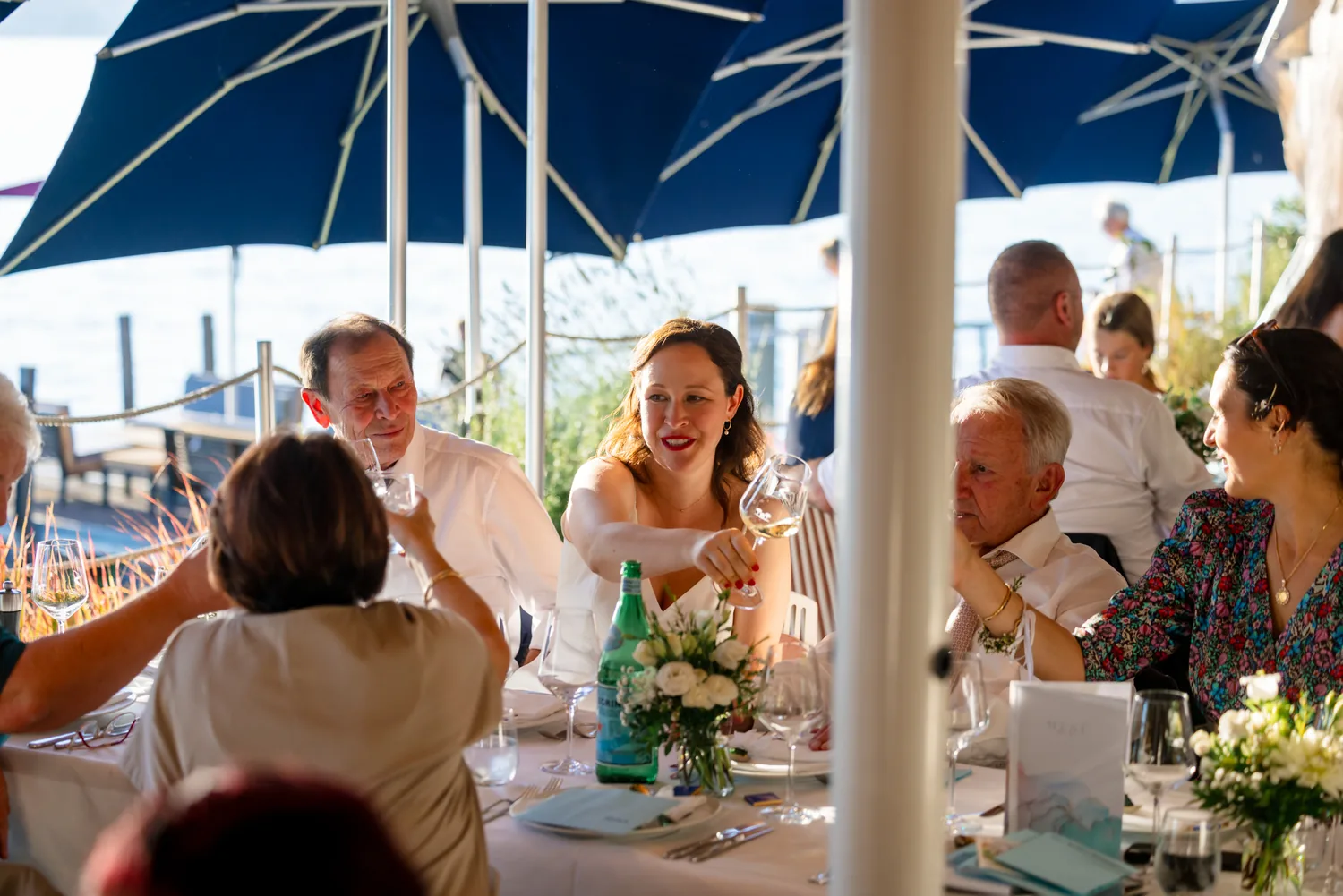 Gäste sitzen beim Abendessen unter blauen Sonnenschirmen direkt am Zürichsee