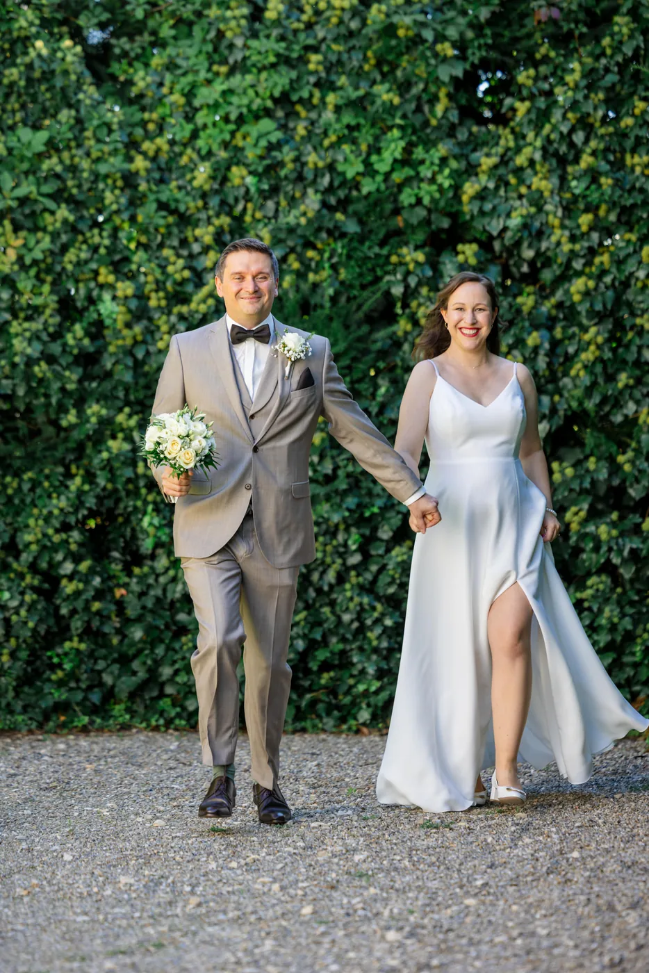 Brautpaar geht Hand in Hand über den Kiesweg vor der hohen Hecke im Garten des Erlenguts