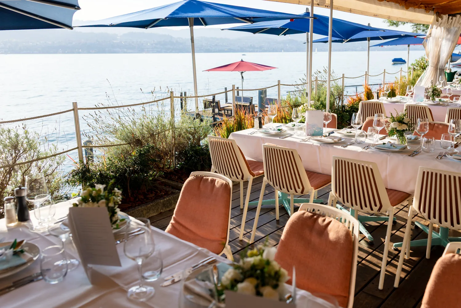 Lange gedeckte Tische auf der Terrasse am Zürichsee, blaue Sonnenschirme