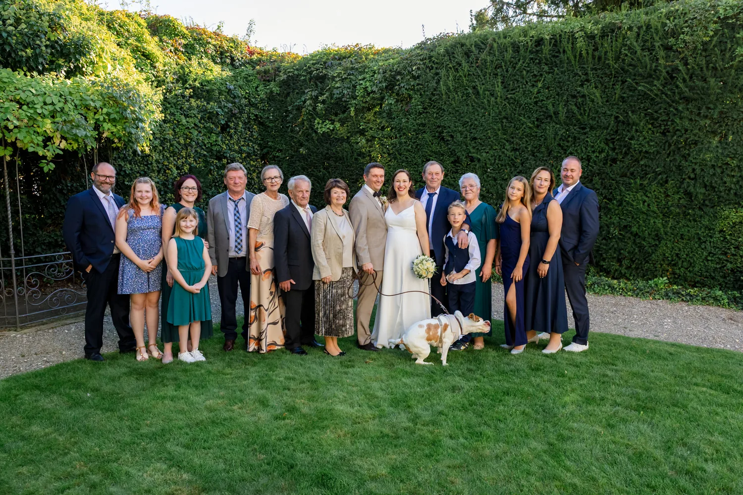 Die ganze Hochzeitsgesellschaft mit Hund vor der hohen Hecke im Garten des Erlenguts