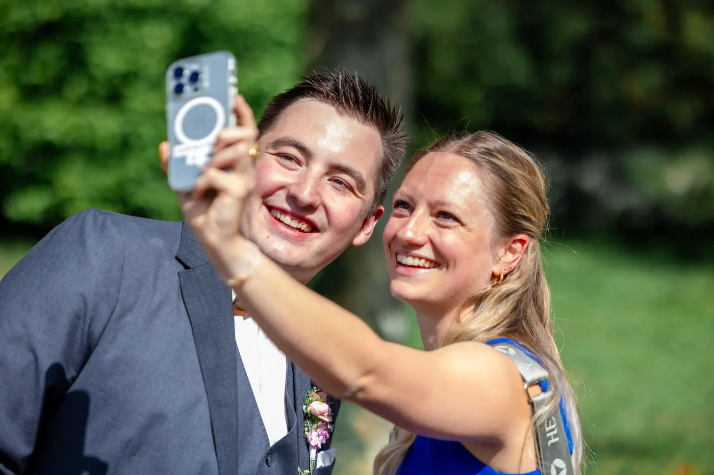 Ein Gast macht mit dem lachenden Bräutigam ein Selfie im Grünen