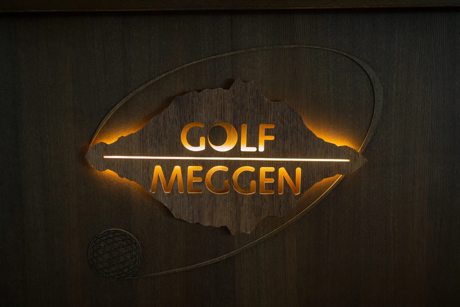 Beleuchtete Wandtafel mit dem Schriftzug Golf Meggen und einer Bergsilhouette auf dunklem Holz
