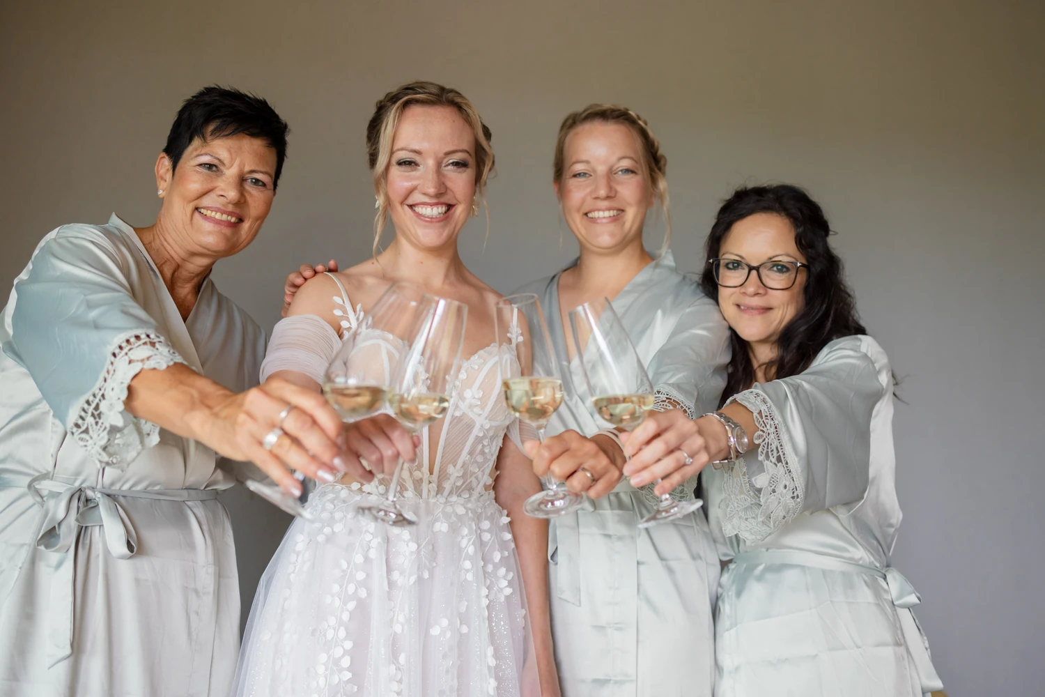 Braut und drei Frauen in Morgenmänteln strecken ihre Gläser in die Kamera