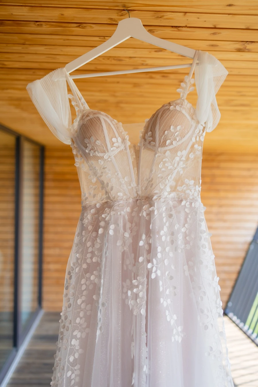 Brautkleid mit Blütenapplikationen hängt an der hellen Holzwand des Zimmers