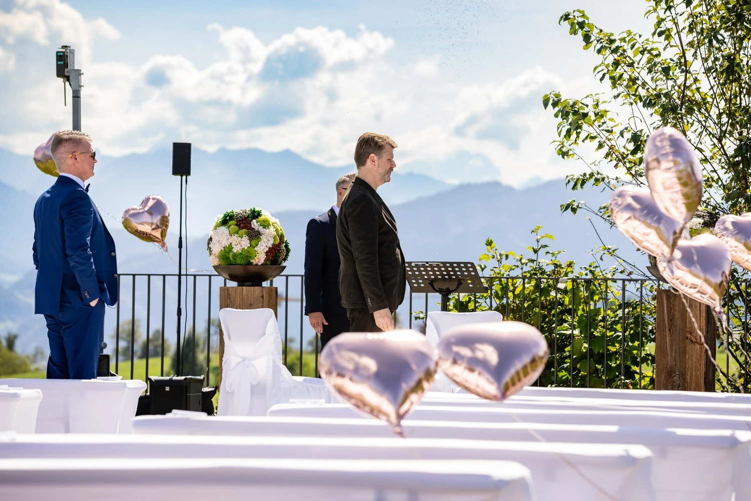 Rednerpult mit Blumenschmuck und Lautsprecher am Rand der Terrasse, dahinter das Bergpanorama