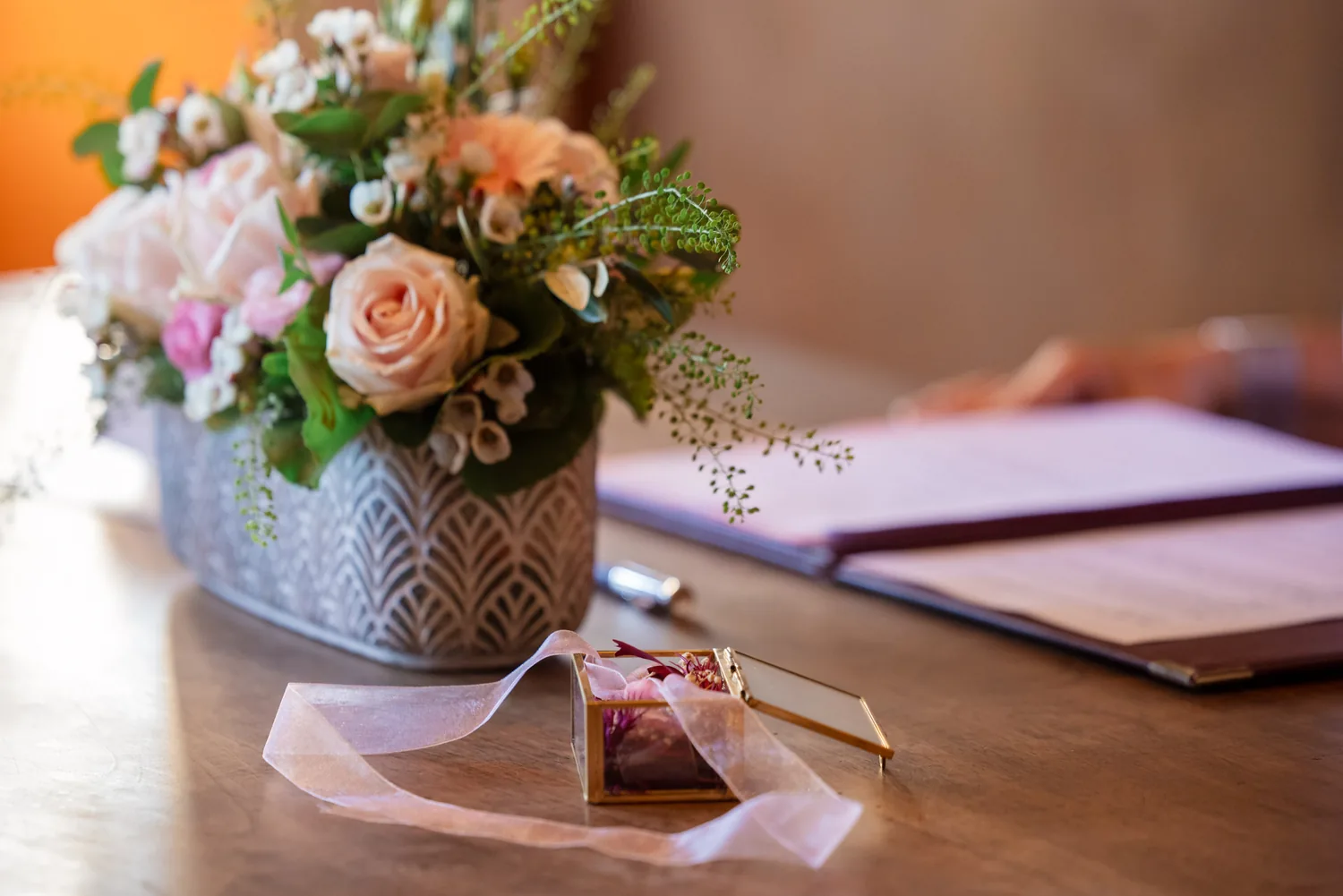Blumenschmuck und eine kleine Ringschatulle mit Blütenblättern auf dem Holztisch im Trauzimmer