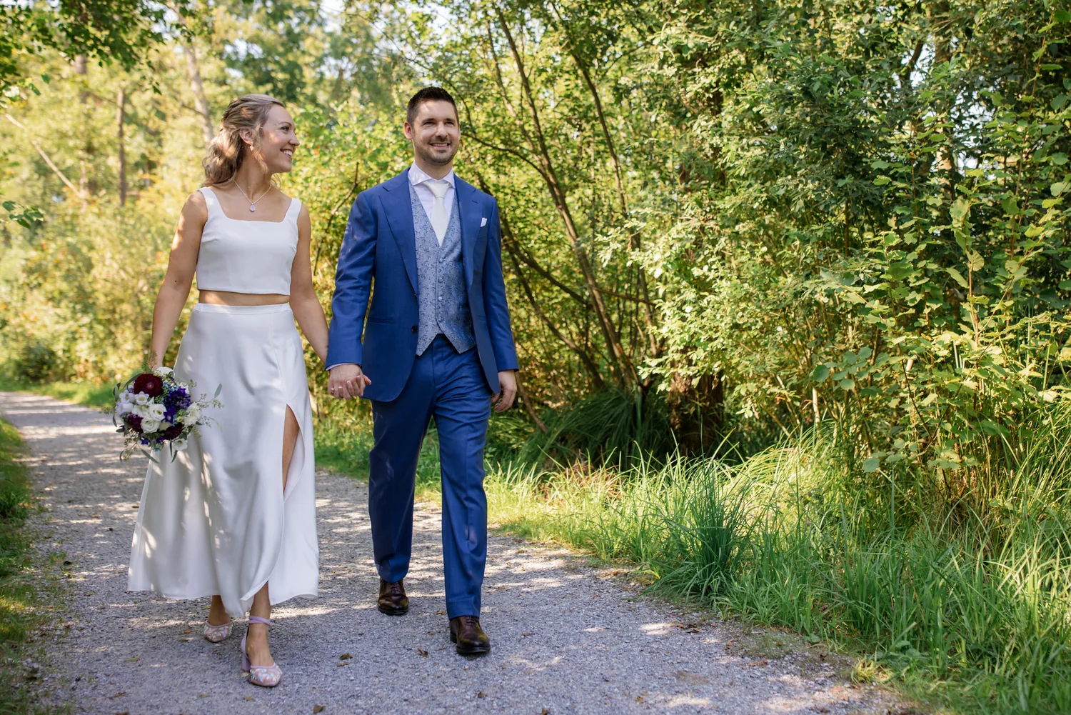 Brautpaar geht Hand in Hand einen Weg entlang, weg vom Schloss