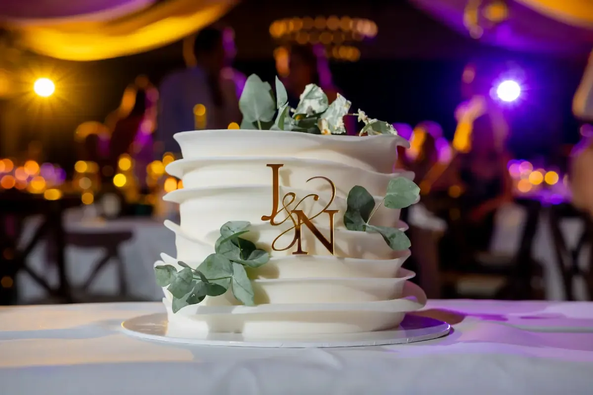 Dreistöckige weisse Hochzeitstorte mit Eukalyptus und einem goldenen Monogramm aus zwei Buchstaben