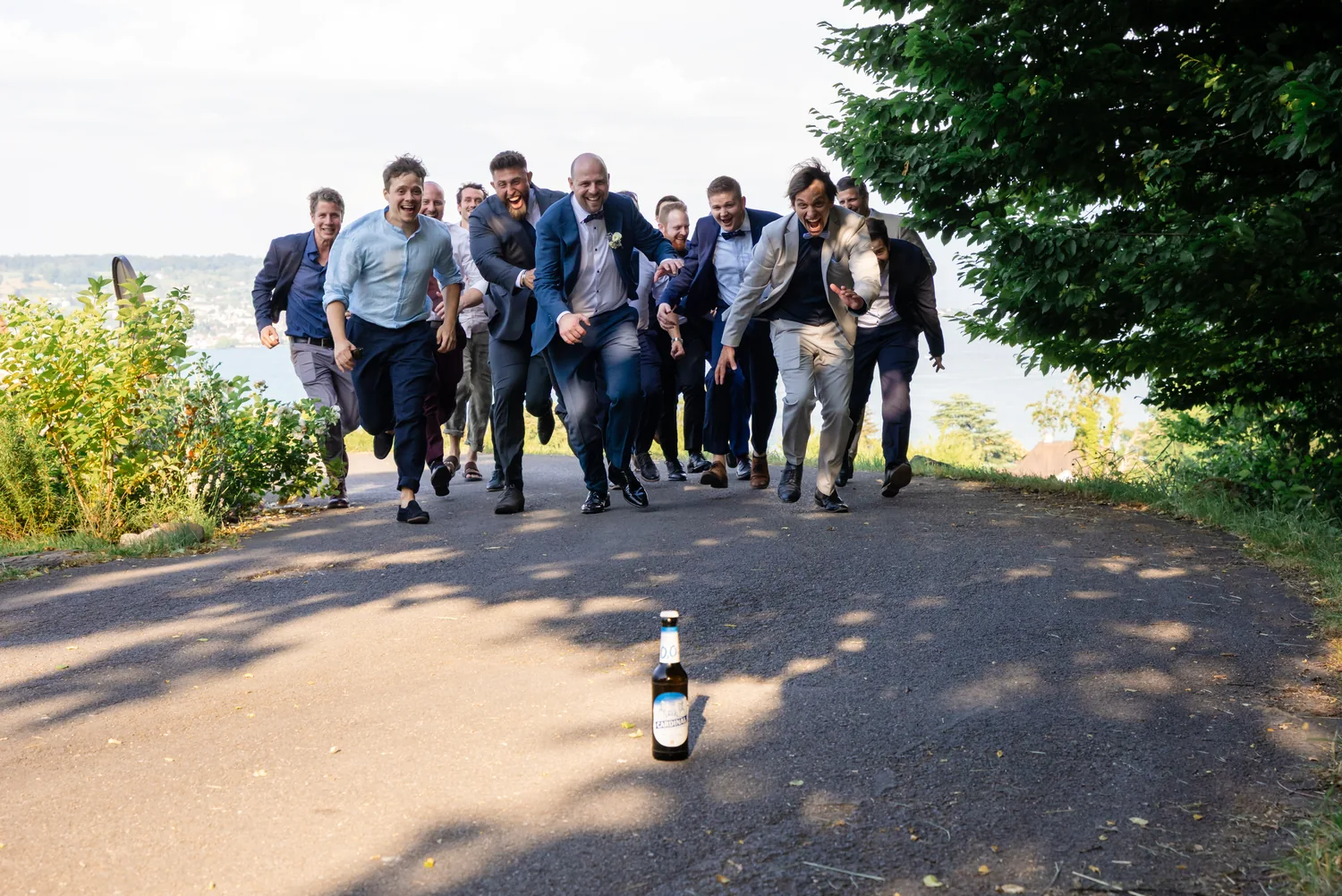 Eine Gruppe Männer in Anzügen rennt lachend einen Weg hinunter auf die Kamera zu, im Hintergrund der Zürichsee