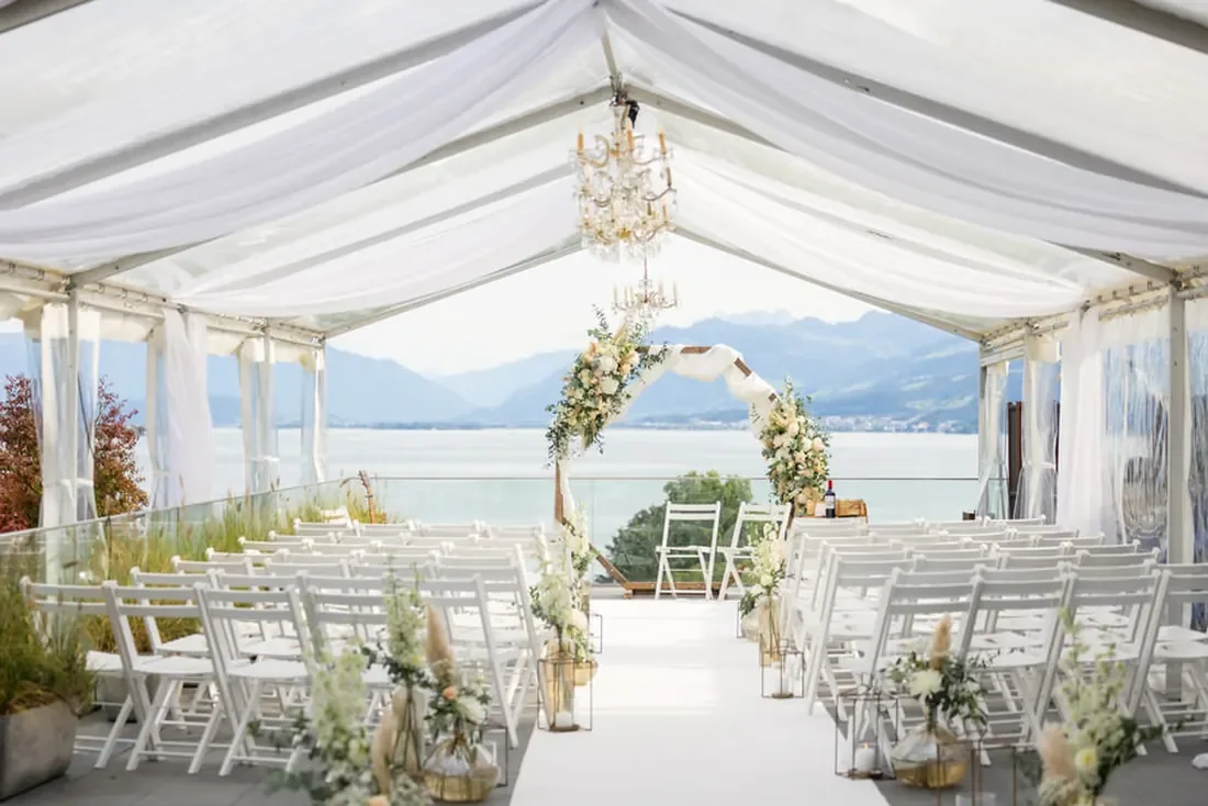 Weisses Zelt mit Kronleuchter und Blumenbogen, offen zum Zürichsee, davor Stuhlreihen für die Zeremonie