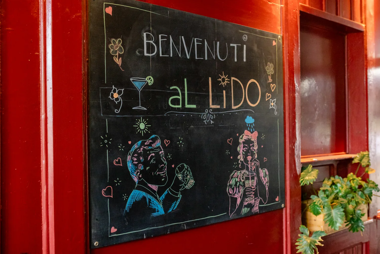 Handgeschriebene Kreidetafel mit der Aufschrift Benvenuti al Lido am roten Eingang
