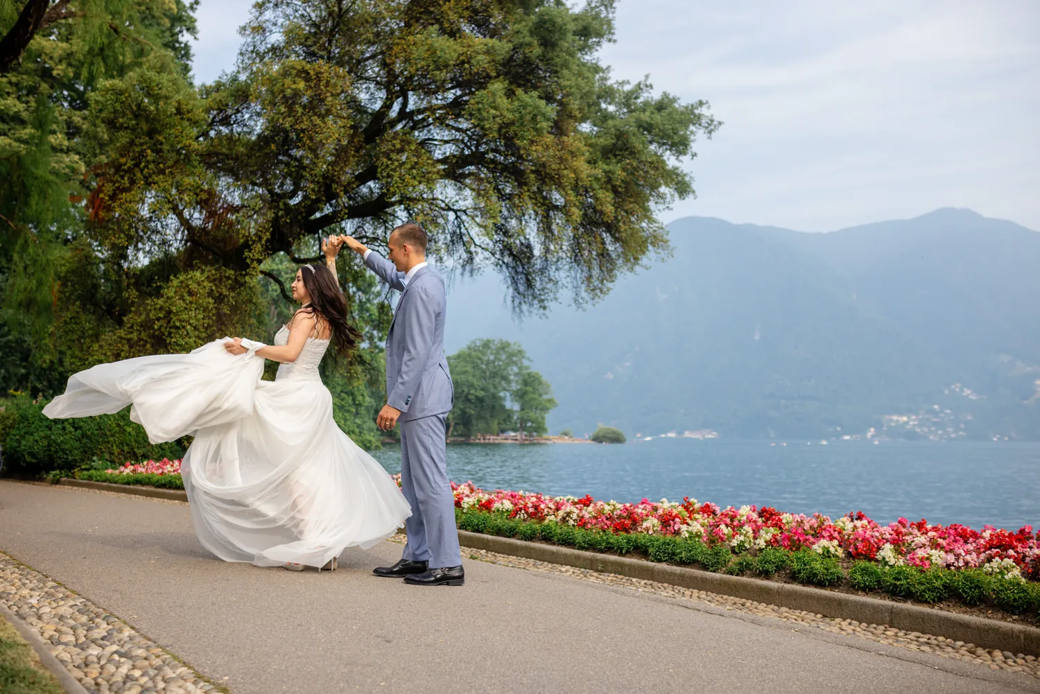 Braut wirbelt ihr Kleid am Blumenbeet, dahinter der See