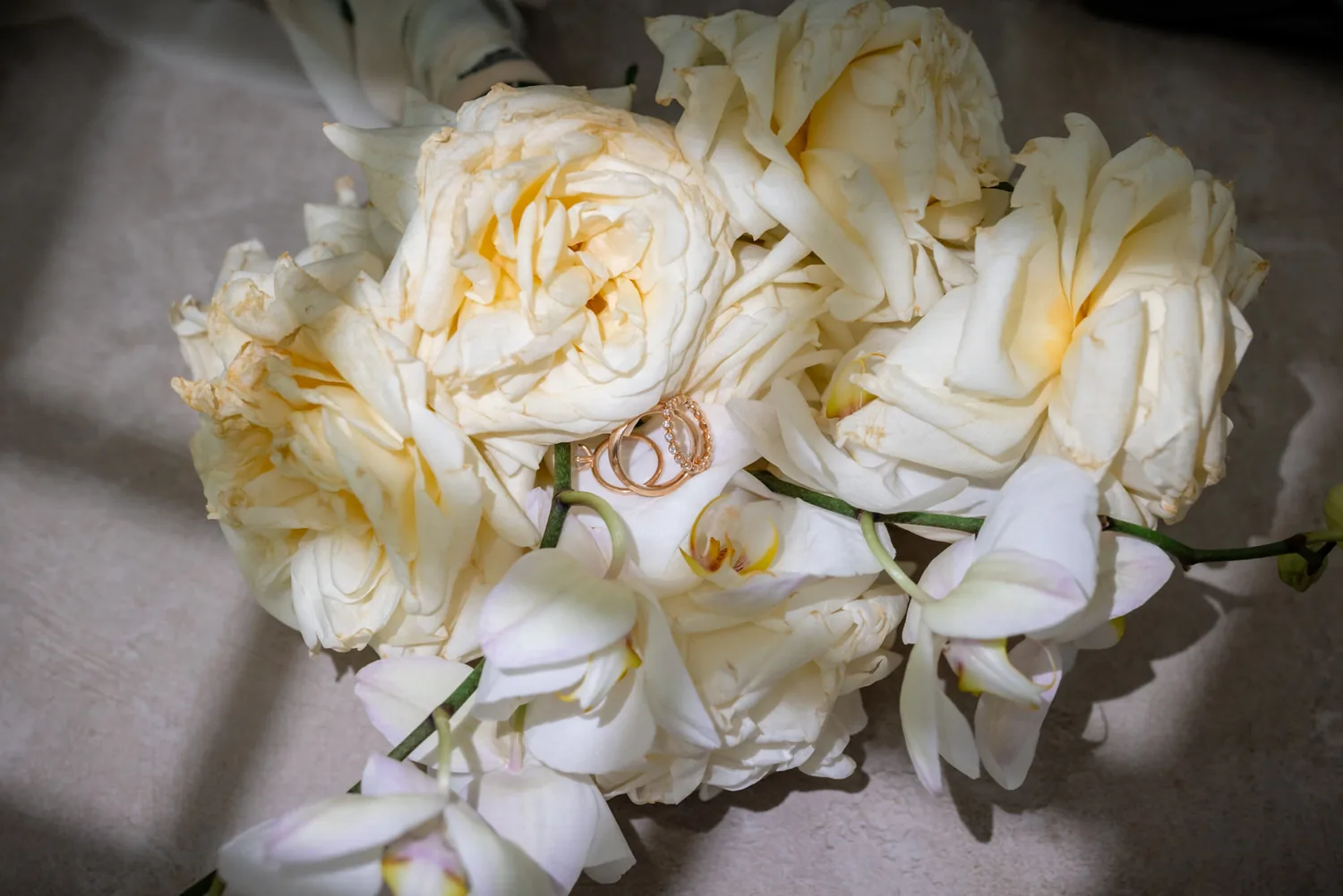 Die beiden Eheringe liegen auf dem Brautstrauss aus weissen Rosen und Orchideen