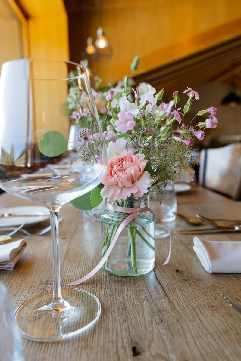 Blumenstrauss in einem Einmachglas neben einem Weinglas auf der Tafel