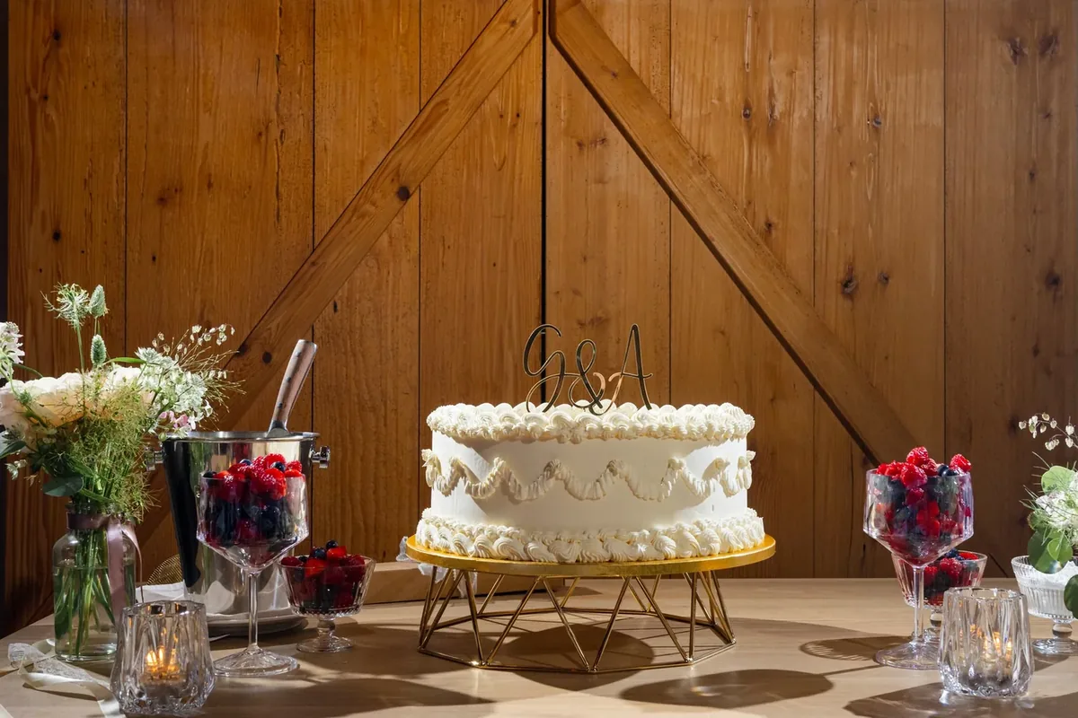 Weisse Torte auf einem goldenen Ständer vor der hölzernen Schiebetür, daneben Beeren im Glas und das Messer
