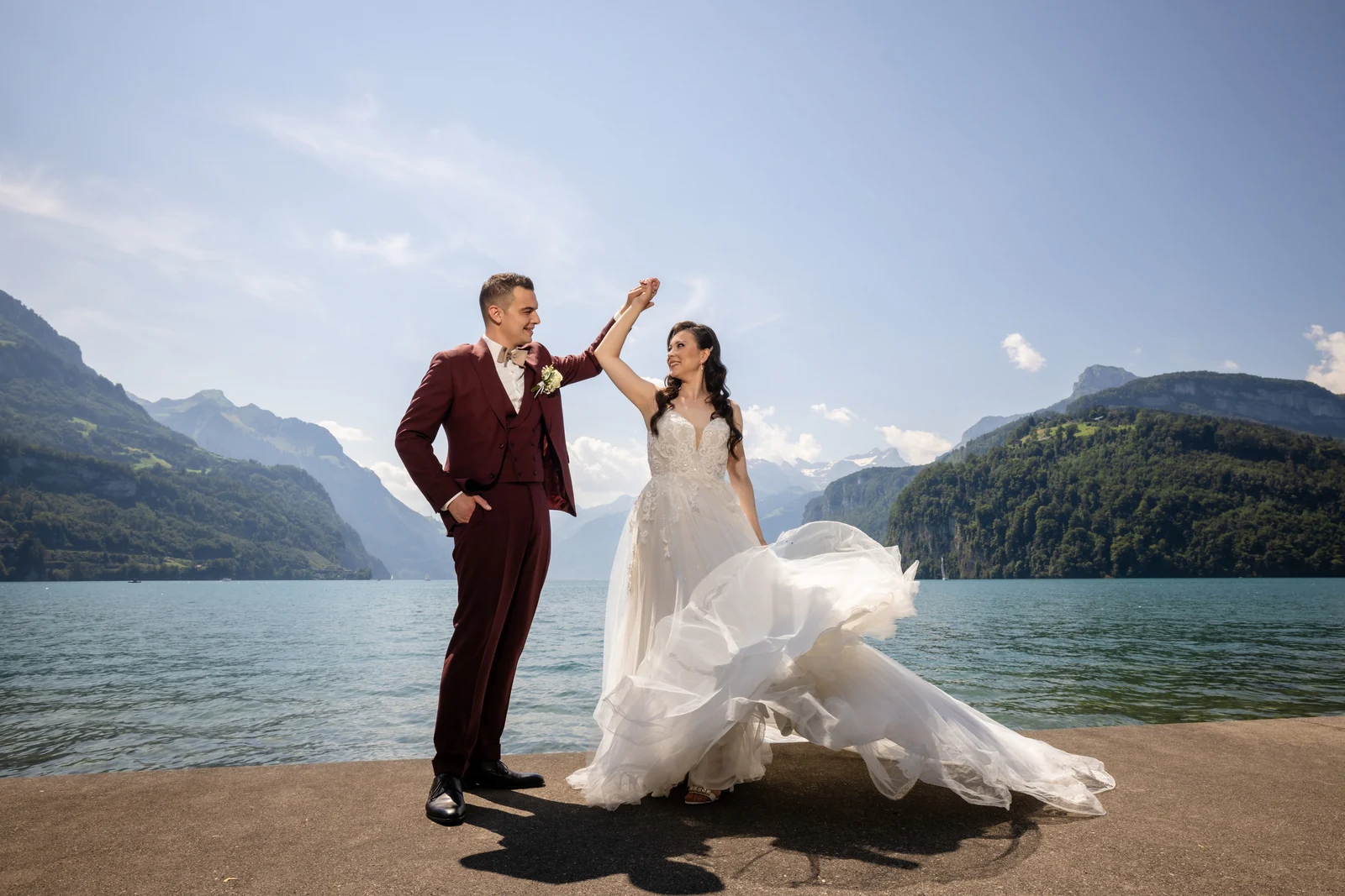 Bräutigam dreht die Braut am Ufer des Urnersees, ihr Kleid schwingt weit aus, dahinter die Berge