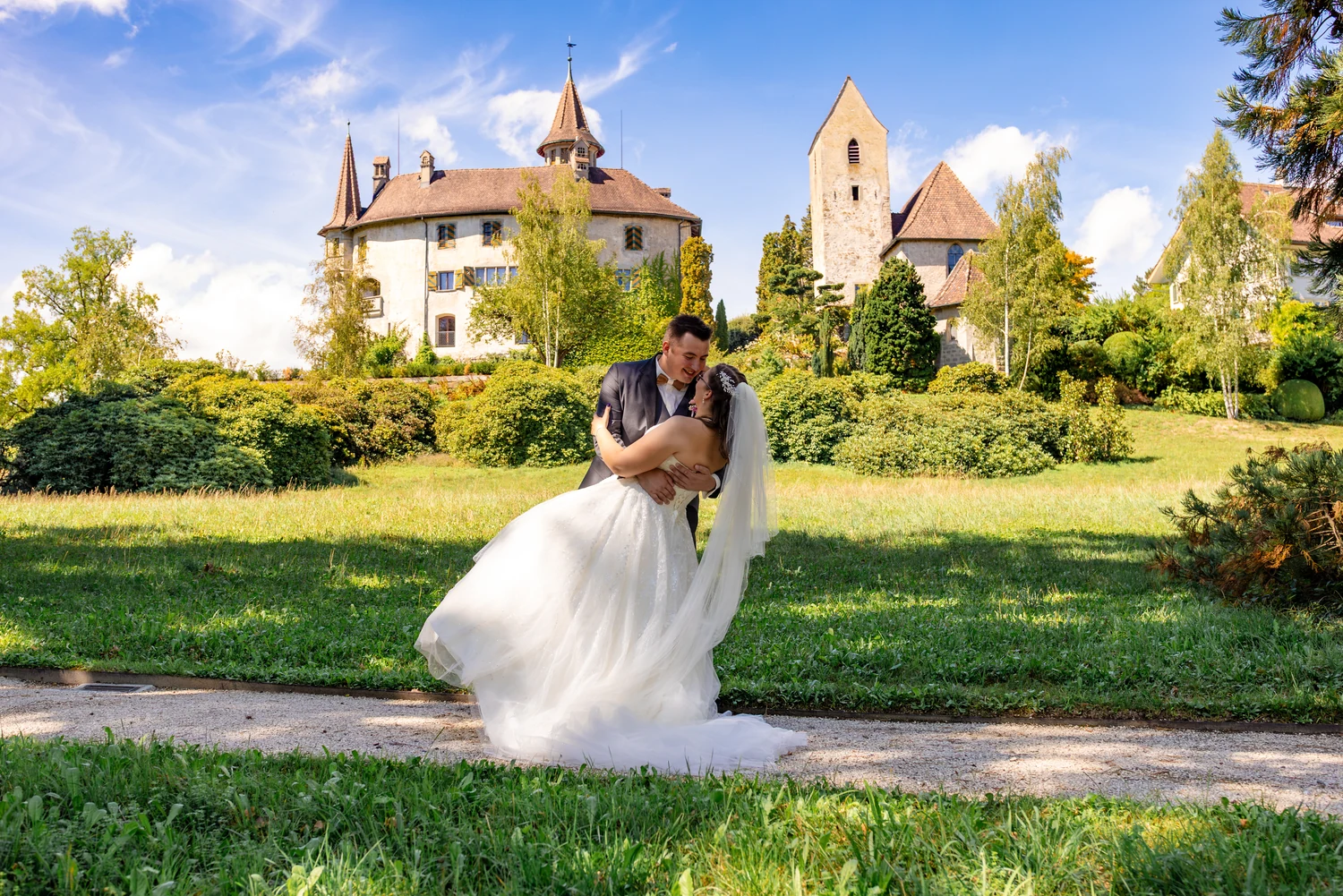 Bräutigam neigt die Braut zum Kuss auf einer Wiese, im Hintergrund ein Schloss mit Türmchen
