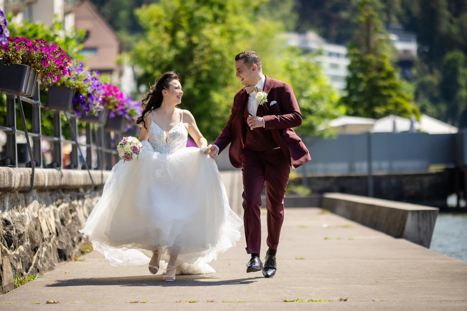 Brautpaar rennt lachend Hand in Hand über eine Seepromenade, die Braut rafft ihr Kleid