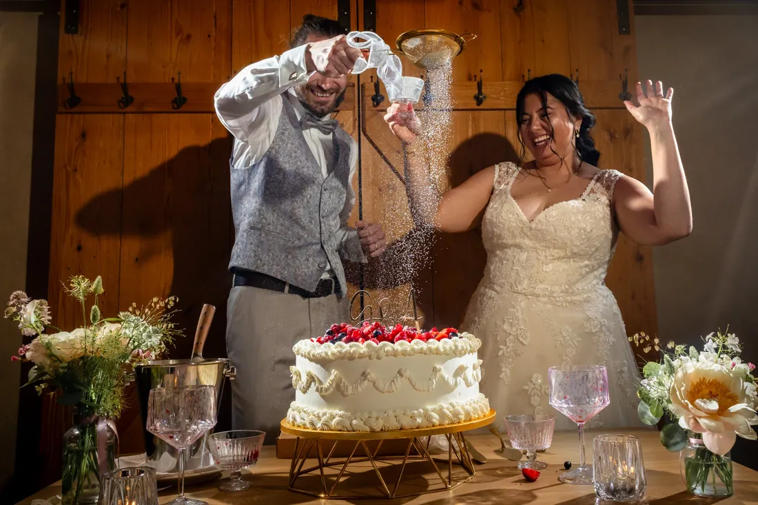 Am Abend: Das Brautpaar bestäubt die Hochzeitstorte lachend mit Puderzucker