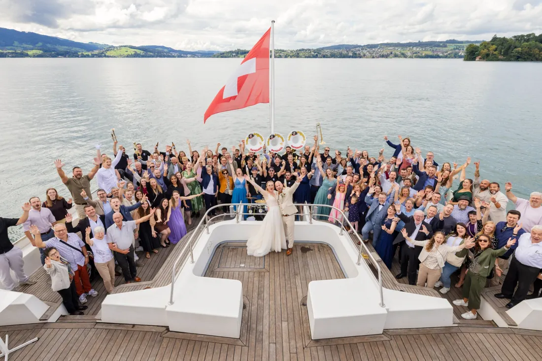 Gruppenbild auf dem Schiffsdeck: Die ganze Hochzeitsgesellschaft jubelt mit dem Brautpaar, dahinter der See