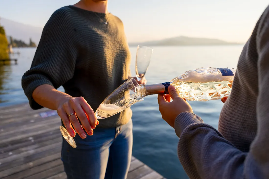 Verlobungsshooting auf einem Steg am See: Champagner wird eingeschenkt, am Finger glänzt der Verlobungsring