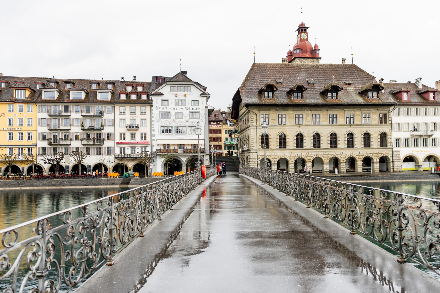 Menschenleere Fussgängerbrücke bei Regen, das nasse Pflaster spiegelt die Altstadthäuser und das Rathaus am anderen Ufer