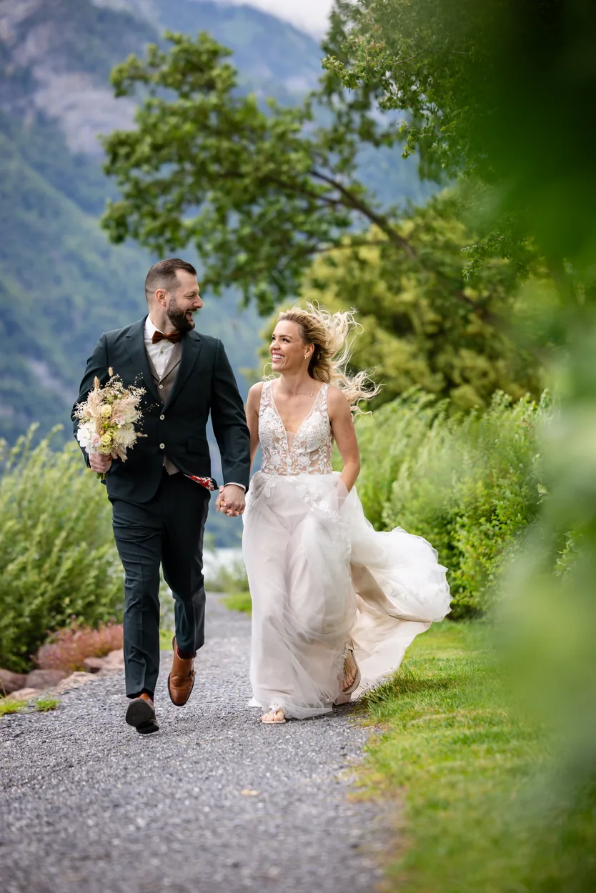 Brautpaar geht Hand in Hand einen Kiesweg entlang, das Kleid schwingt zur Seite
