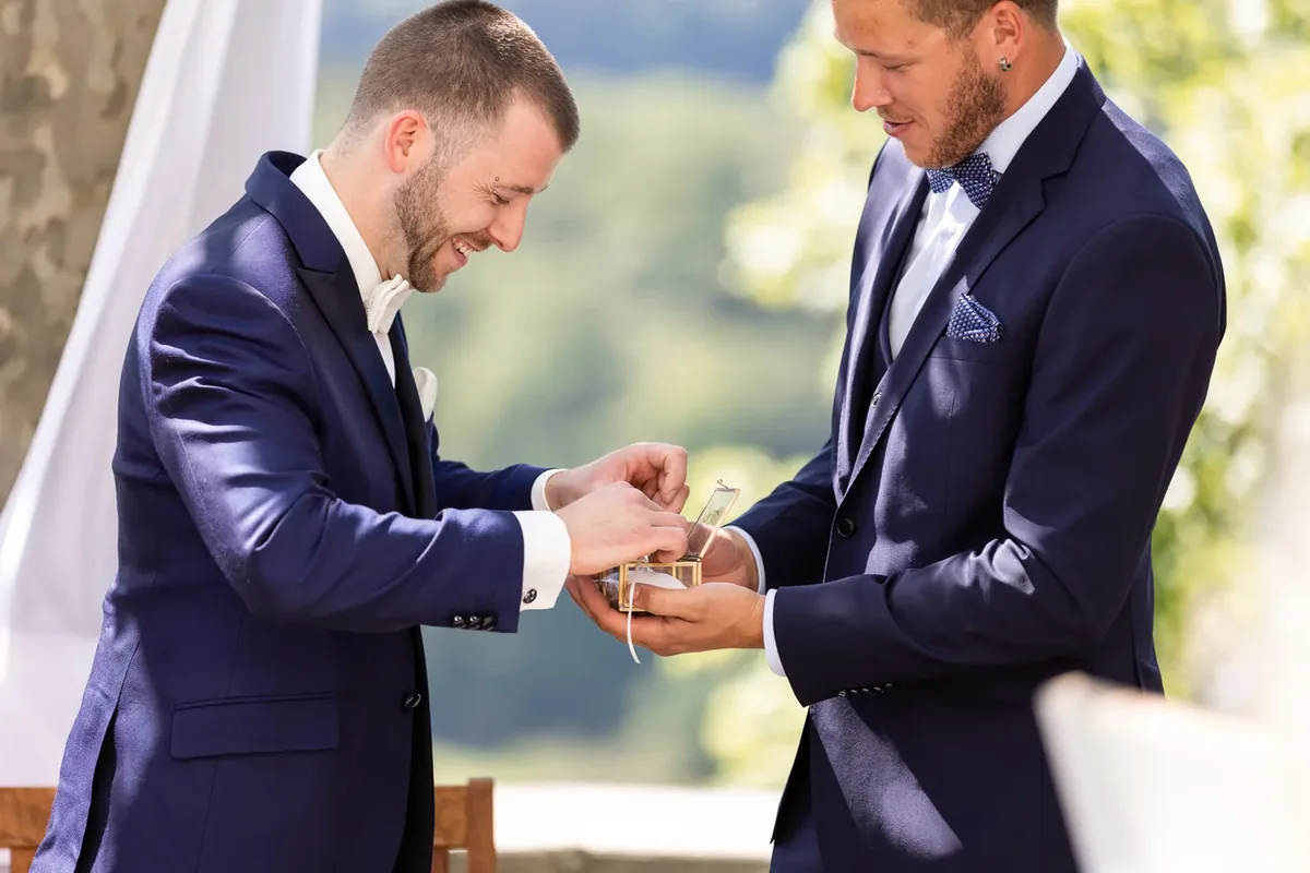 Der Bräutigam und ein Trauzeuge öffnen gemeinsam eine kleine goldene Ringschatulle