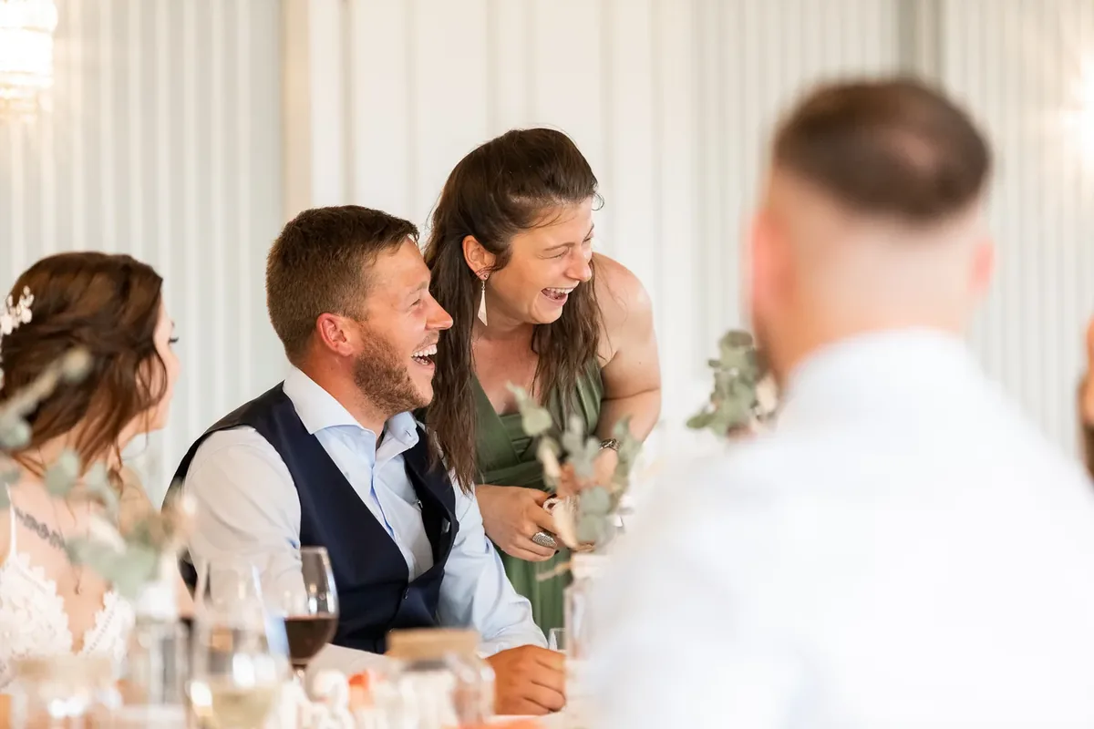 Der Bräutigam und eine Frau im grünen Kleid lachen am Brauttisch