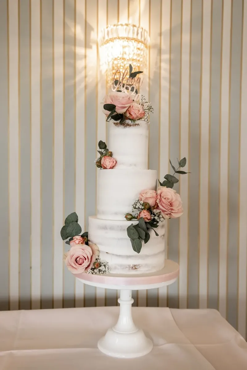 Die dreistöckige Torte auf einem weissen Ständer vor gestreifter Wand