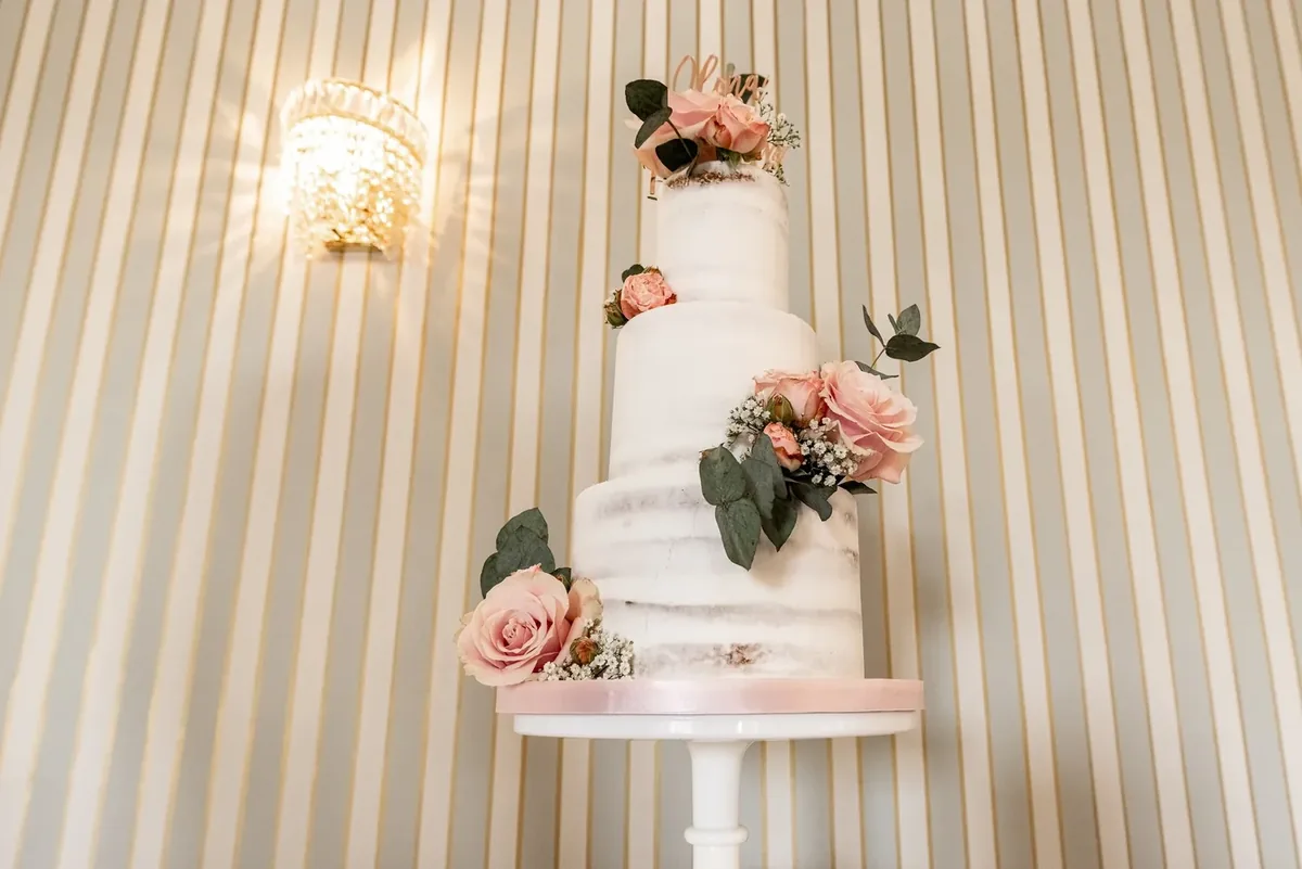 Dreistöckige Hochzeitstorte mit Rosen unter einer Wandlampe