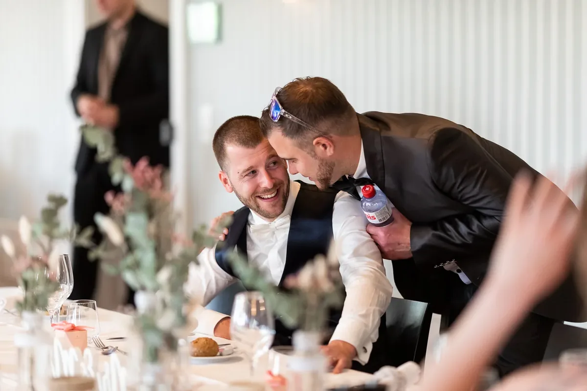 Ein Gast umarmt den lachenden Bräutigam am gedeckten Tisch