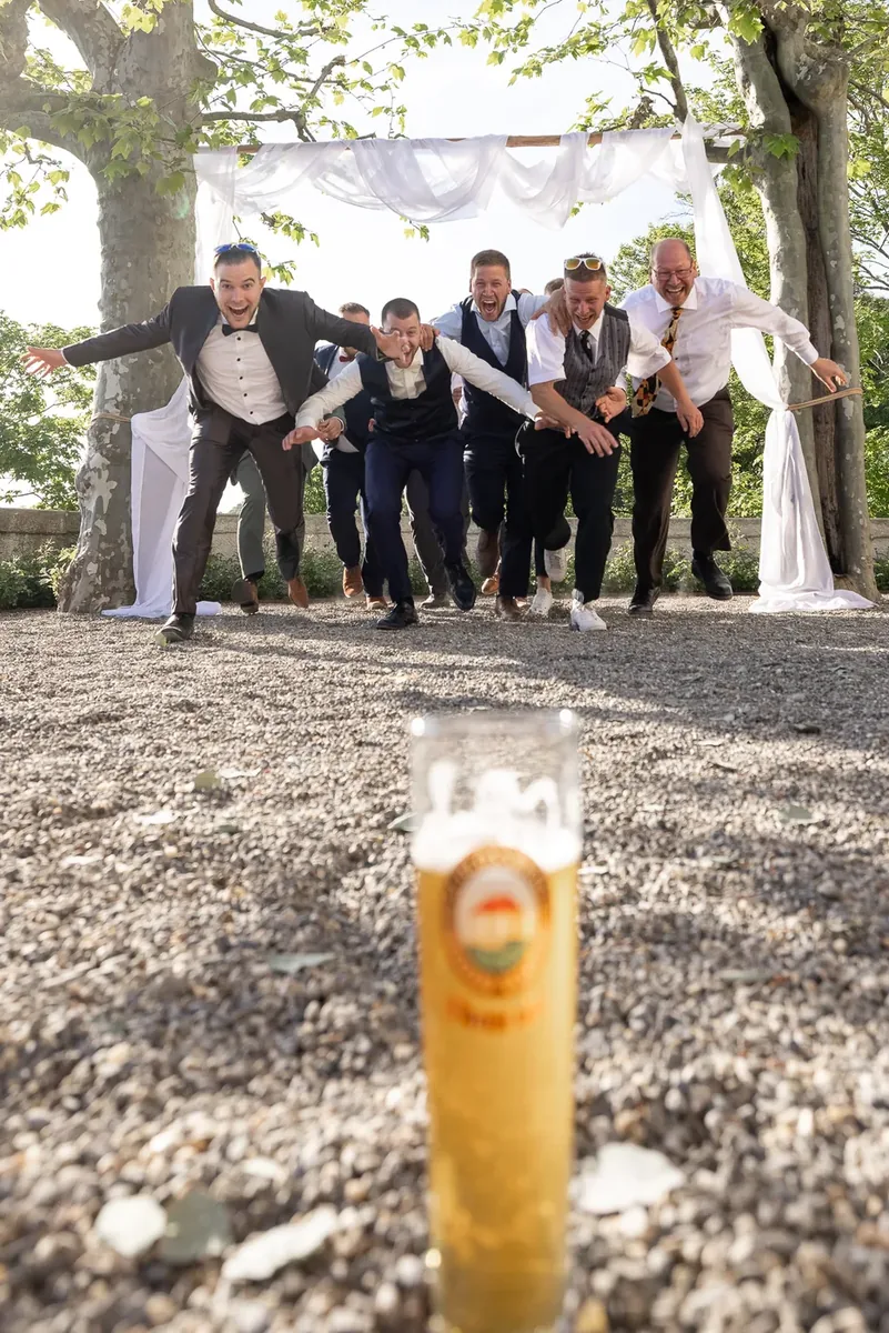 Eine Gruppe Männer sprintet unter dem Traubogen hindurch auf ein Bierglas im Vordergrund zu