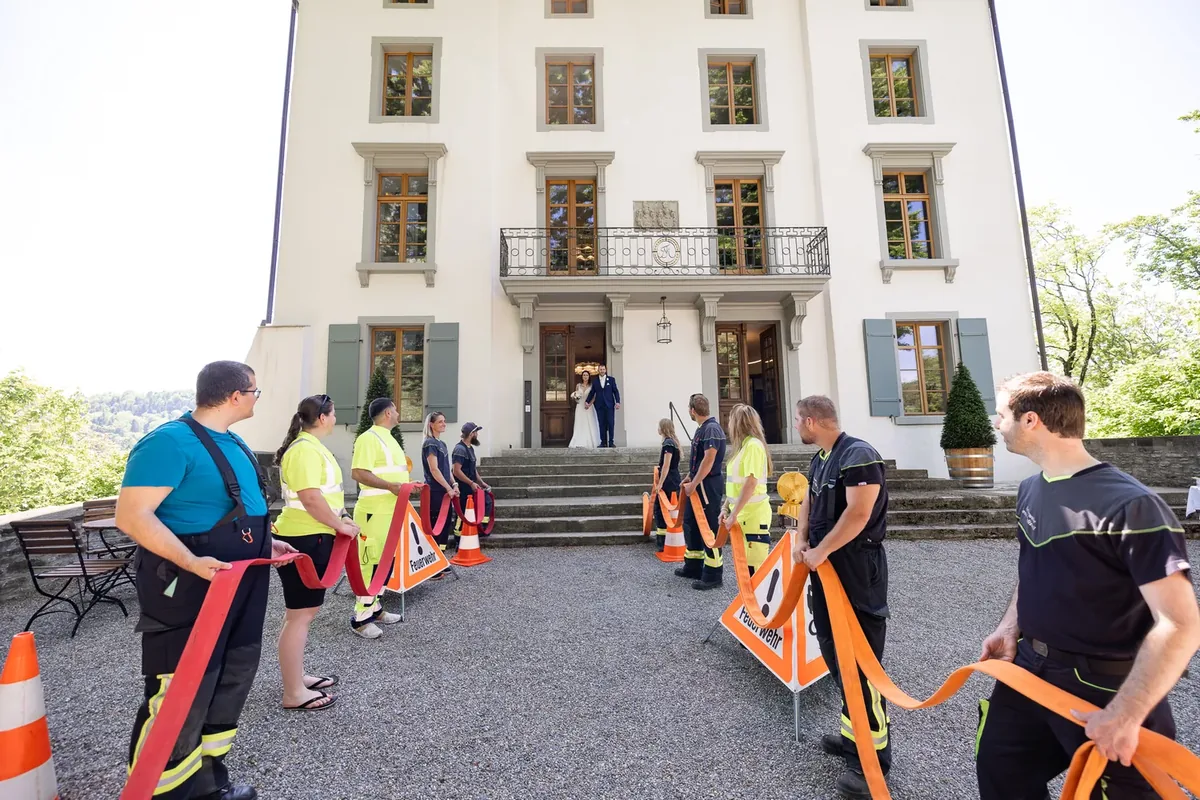 Feuerwehrleute bilden mit roten Schläuchen und Signaltafeln ein Spalier vor dem Schlosseingang