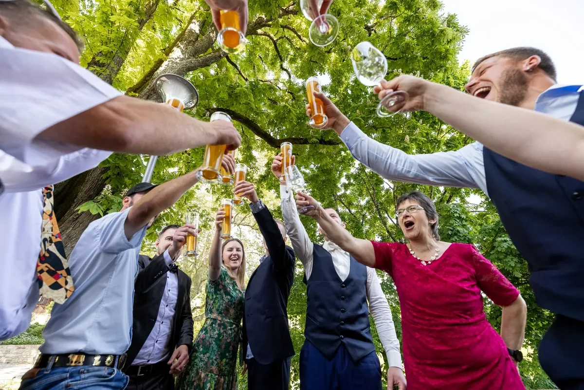 Gäste stossen mit Biergläsern unter dem Baum an