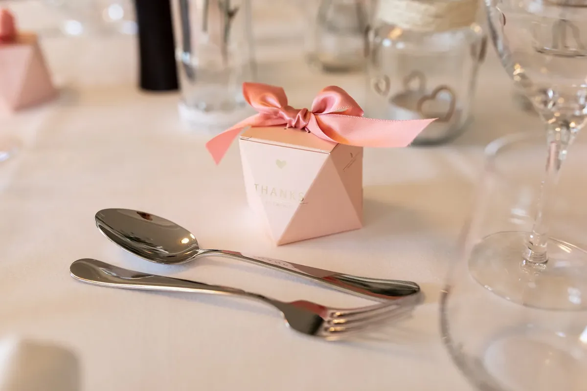 Rosa Gastgeschenk mit Satinschleife neben Löffel und Gabel